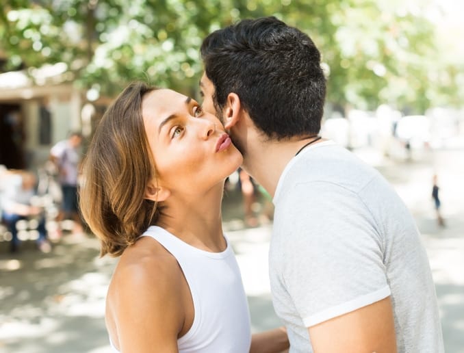 cheerful adult man and woman meeting and kissing on the street in summer